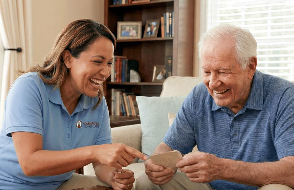 CaraVita caregiver in a light blue polo laughing with an older man over a card game at home
